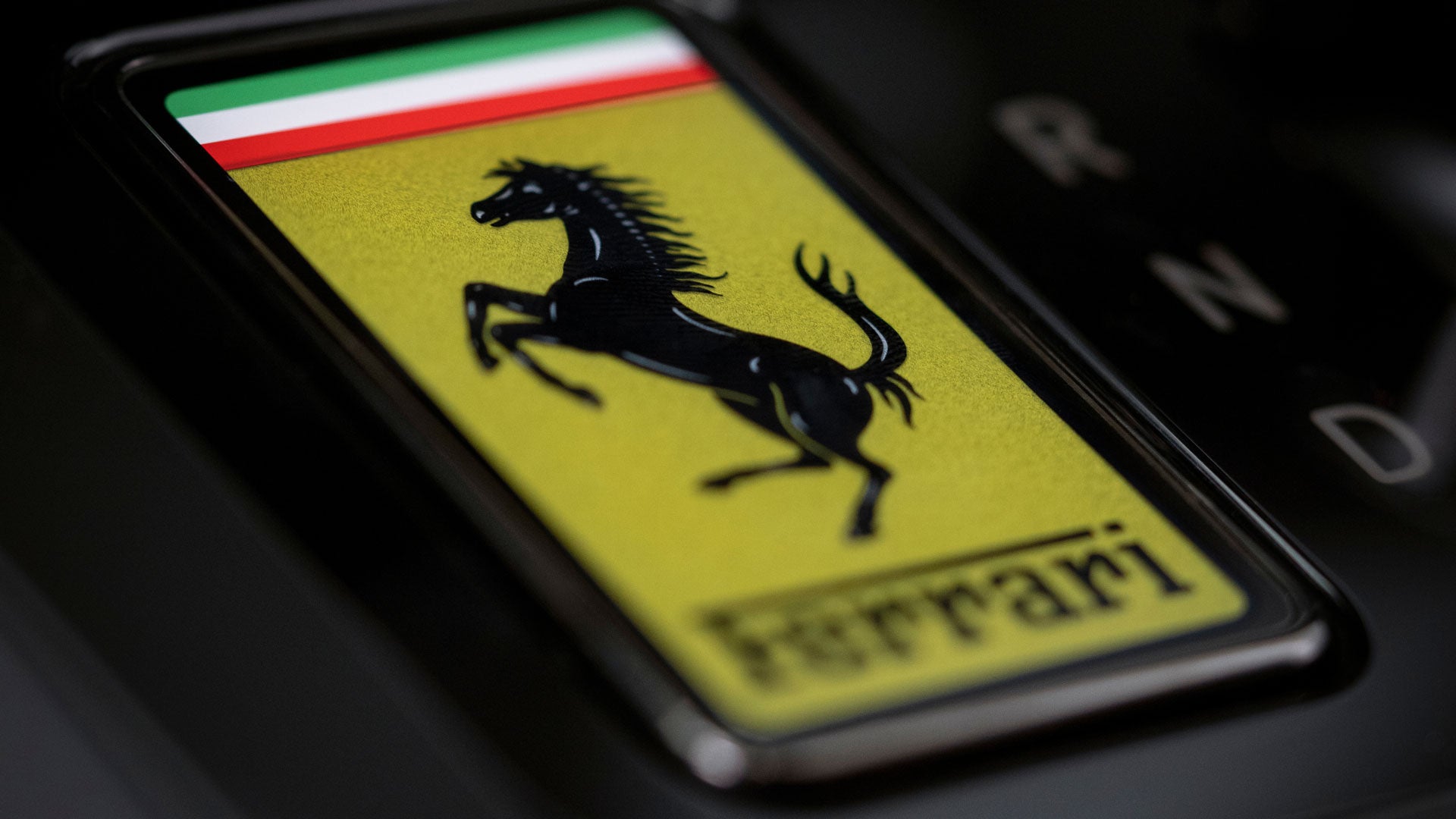 Embossed Ferrari logo on glossy red surface, with a black racing stripe featuring a Prancing Horse emblem.